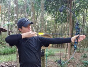 Um homem segurando o arco e a flecha, preparado para atirar, mirando o alvo que não aparece na imagem.